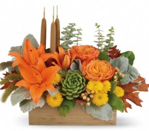 gorgeous centerpiece arrangement features orange rose, orange asiatic lilies, yellow cushion spray chrysanthemums, peach hypericum, millet, cattails and a succulent plant, and finished with dusty miller, spiral eucalyptus and lemon leaf.