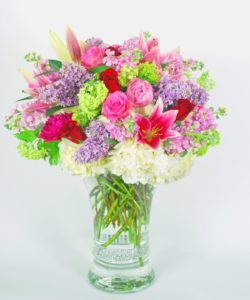 Pink and red roses with lilies and purple and white hydrangeao and green accents in a glass vase