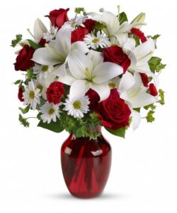 Red roses and carnations are exquisitely arranged with white asiatic lilies and chrysanthemums in a ruby red glass vase