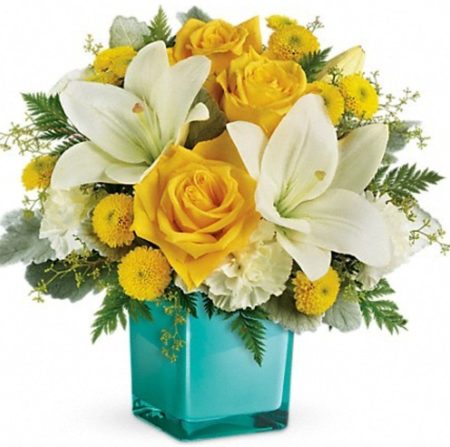 This cheerful bouquet features yellow roses, white asiatic lilies, white carnations, yellow button spray chrysanthemums, seeded eucalyptus, dusty miller and leatherleaf fern. Delivered in a glass cube.