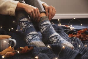 Woman wearing knitted socks on warm plaid indoors, closeup. Cozy season